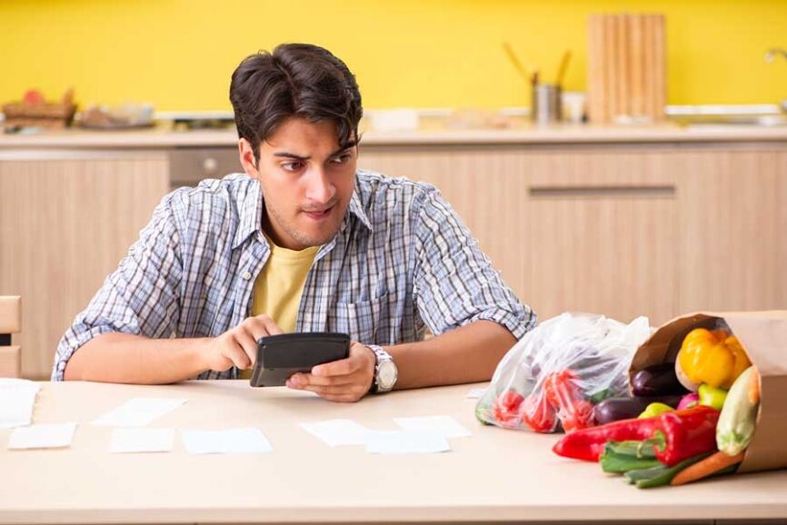Young man calculating expences for vegetables in kitchen Скъпо ли е кето храненето.
